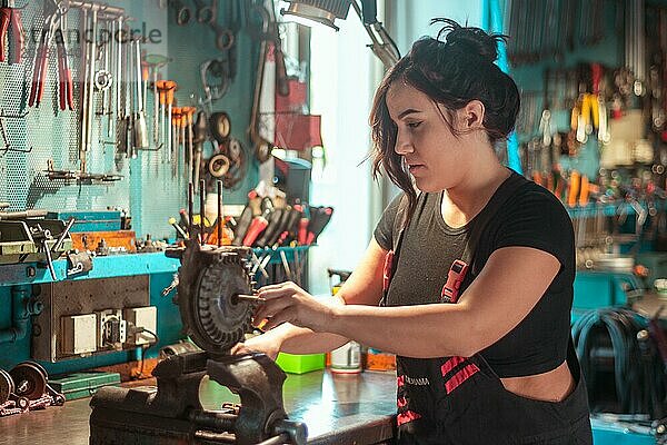 Eine Frau arbeitet aufmerksam an einer mechanischen Arbeit an einer aufgeräumten Werkbank  eine komplette Werkzeugtafel im Hintergrund mit Bokeh Effekt  traditionelle Männerarbeit von Mixed race latino woman