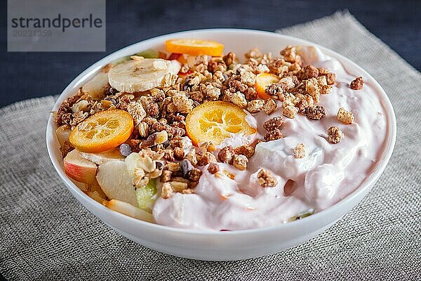 Vegetarischer Salat aus Bananen  Äpfeln  Birnen  Kumquats  Kiwi mit Granola und Joghurt auf schwarzem woodem Hintergrund  Nahaufnahme  selektiver Fokus