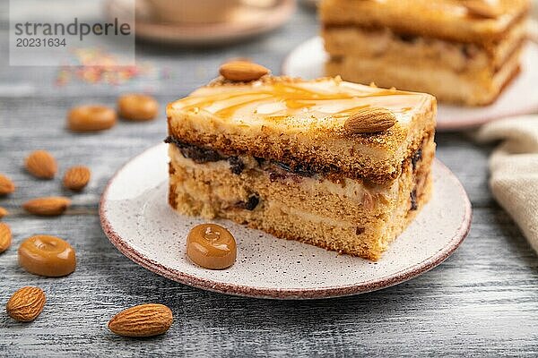 Honigkuchen mit Milchcreme  Karamell  Mandeln und einer Tasse Kaffee auf einem grauen Holzhintergrund und Leinenstoff. Seitenansicht  Nahaufnahme  selektiver Fokus