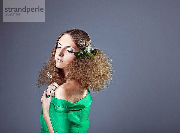Schöne junge Frau in grünem Tuch mit Blättern und Kamille im Haar