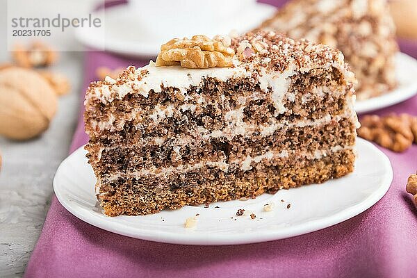 Hausgemachter Kuchen mit Milchcreme und Walnüssen mit einer Tasse Kaffee auf einem grauen Betonhintergrund und lila Textil. Seitenansicht  Nahaufnahme  selektiver Fokus