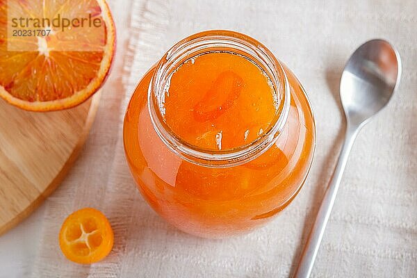 Orangen und Kumquatmarmelade in einem Glas mit frischen Früchten auf einer weißen Leinentischdecke. Hausgemacht  Nahaufnahme