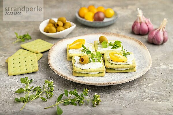 Grüne Cracker Sandwiches mit Frischkäse und Kirschtomaten auf grauem Betonhintergrund. Seitenansicht  Nahaufnahme  selektiver Fokus