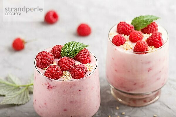 Joghurt mit Himbeere und Sesam in einem Glas und Holzlöffel auf grauem Betonhintergrund. Seitenansicht  Nahaufnahme