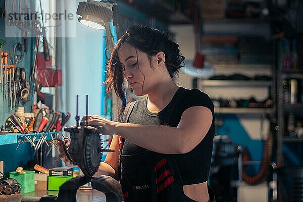 Eine Handwerkerin ist sorgfältig mit Reparaturarbeiten beschäftigt  umgeben von Werkzeugen in ihrem Beruf  eine komplette Werkzeugtafel im Hintergrund mit Bokeh Effekt  traditionelle Männerberufe von Mixed race latino woman