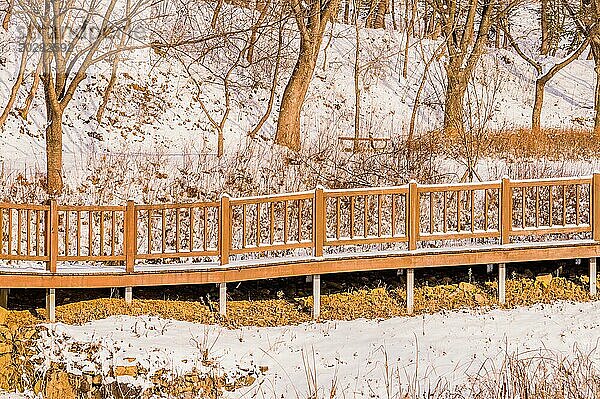 Langer Holzsteg mit verschneitem Geländer in einer ruhigen Winterlandschaft in Südkorea