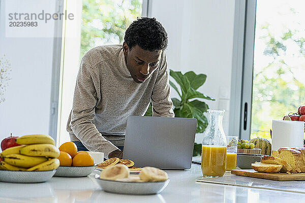 Erwachsener Mann benutzt Laptop  während er an der Küchentheke steht