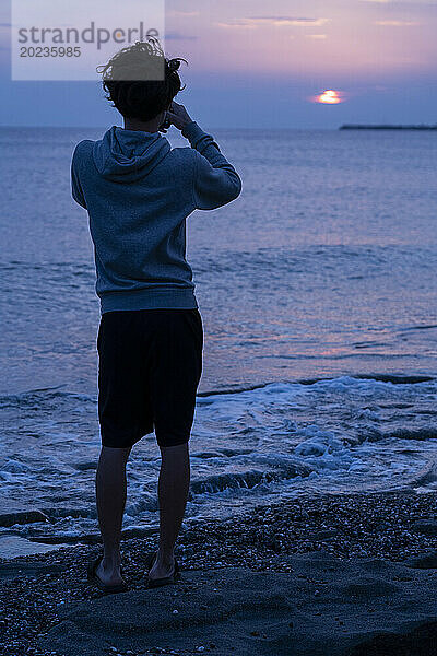 Junger Mensch am Strand mit Blick auf den Horizont bei Sonnenuntergang in der Normandie