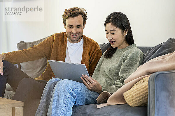Erwachsenes Paar nutzt digitales Tablet  während es auf dem Sofa sitzt