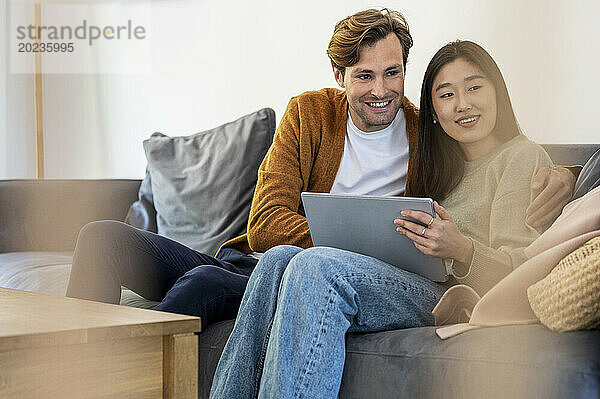 Erwachsenes Paar nutzt digitales Tablet  während es tagsüber auf dem Sofa entspannt