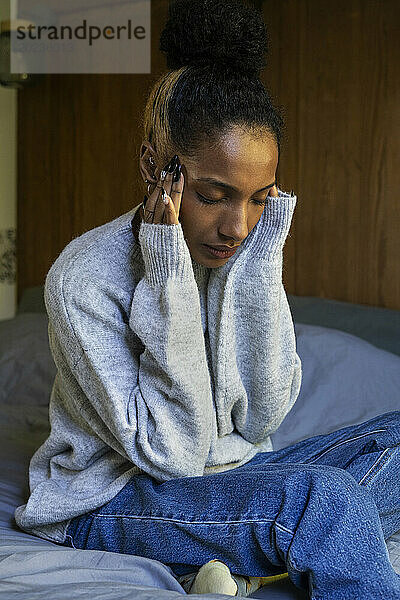 Gestresste junge erwachsene Frau berührt ihren Kopf  während sie im Bett sitzt
