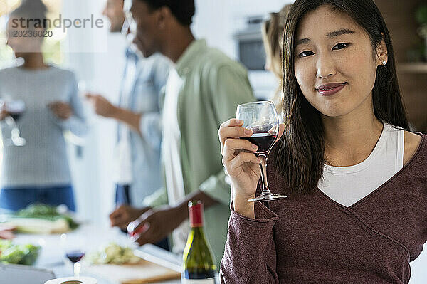 Junge erwachsene Frau hält ein Weinglas in der Hand und blickt in die Kamera