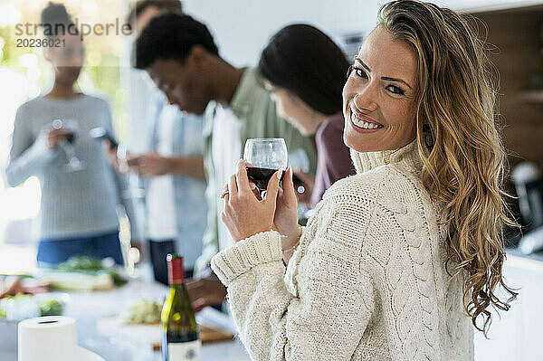 Fröhliche erwachsene Frau blickt zurück in die Kamera  während sie ein Weinglas hält