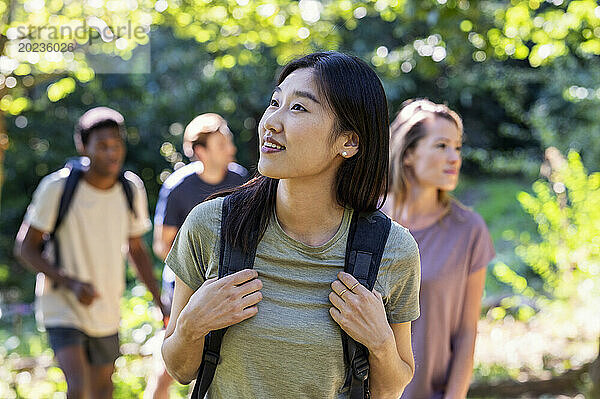 Curious young adult woman looking up while hiking with friends