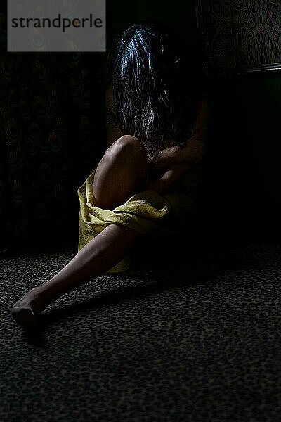Unbekannte Person sitzt im dunklen Raum auf dem Boden