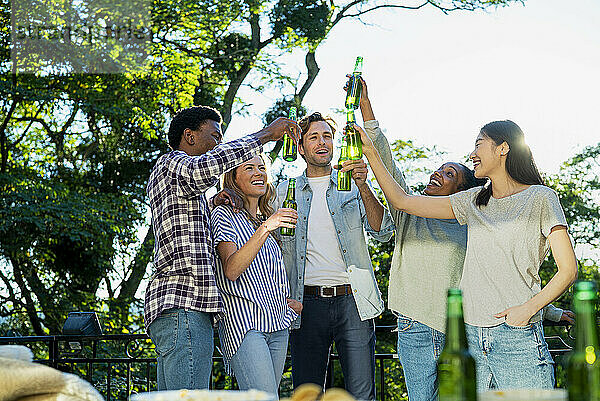 Five friends raising beer bottles while toasting during rooftop party