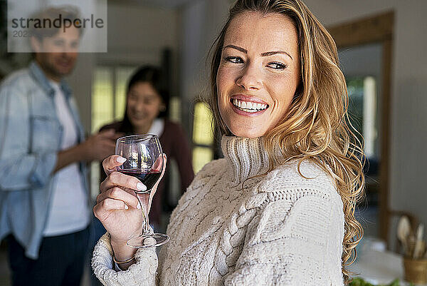 Selbstbewusste Frau hält Weinglas in der Hand  während sie sich mit Freunden auf einer Party trifft