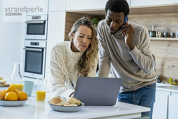 Erwachsenes Paar benutzt Laptop  während es in der Küche steht