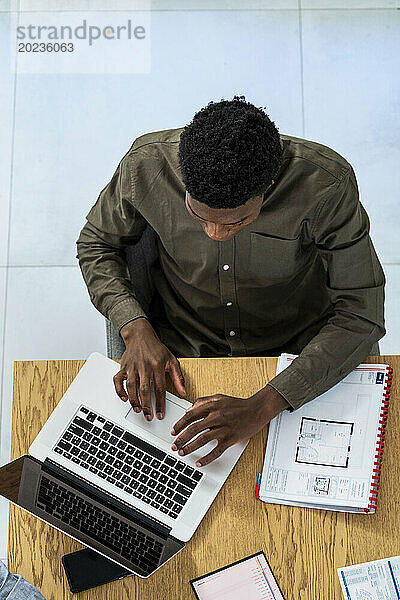 Mitarbeiter einer Werbeagentur benutzt Laptop  während er am Schreibtisch sitzt