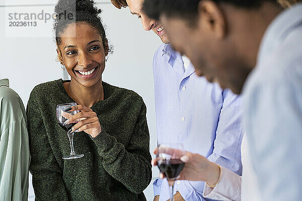 Fröhliche junge erwachsene Frau trinkt Wein während eines Freundestreffens