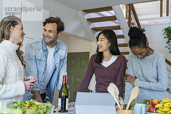 Eine Gruppe von Freunden trinkt Wein  während sie in der Küche hängen
