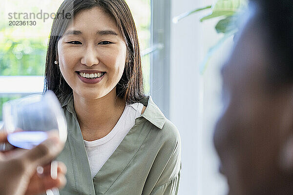 Junge erwachsene Frau lächelt  während sie mit einer Freundin spricht und Wein trinkt