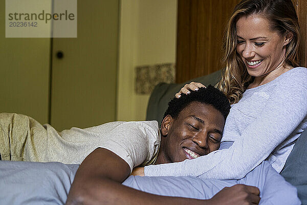 Cheerful man with head on girlfriend's belly while embracing on bed