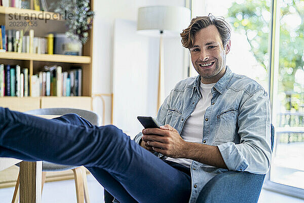 Geschäftsmann benutzt Smartphone  während er auf einem Stuhl sitzt und die Füße auf dem Tisch hat