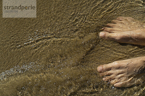 Unidentified person's feet inside running water at beach