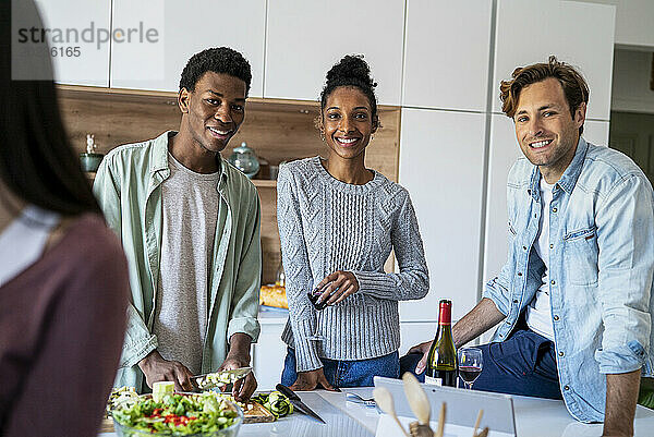 Group of friends drinking wine while hanging on kitchen looking at the camera