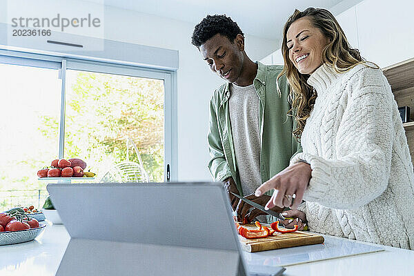 Paar schaut sich Kochrezept auf digitalem Tablet an  während es an der Küchentheke steht