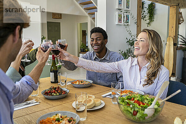 Eine Gruppe von Freunden stößt beim Abendessen im Esszimmer mit Weingläsern an