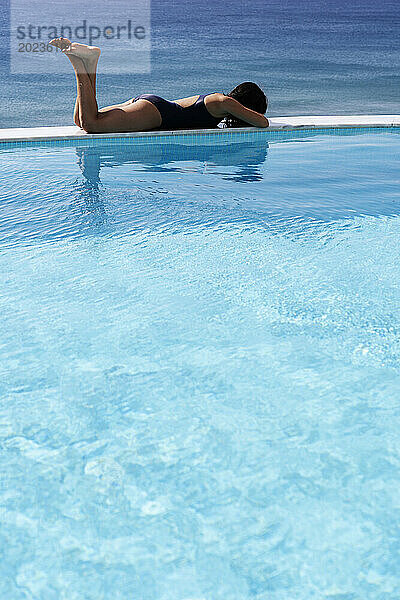 Junge Frau liegt am Schwimmbadrand in der Nähe des Meeres