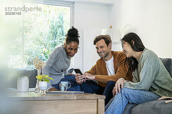 Eine kleine Gruppe von Freunden versammelte sich im Wohnzimmer  während sie ihr Smartphone benutzten