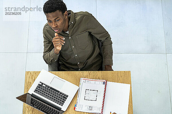 Zenitaler Blick auf einen nachdenklichen Geschäftsmann  der am Schreibtisch sitzt und am Laptop arbeitet
