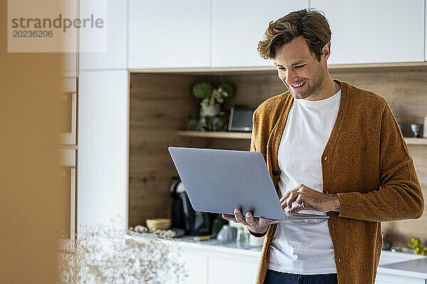 Adult man using laptop while standing in kitchen