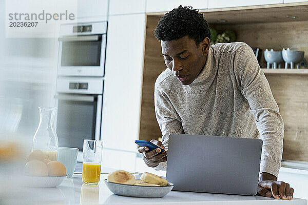 Erwachsener Mann benutzt Smartphone  während er an der Küchentheke steht