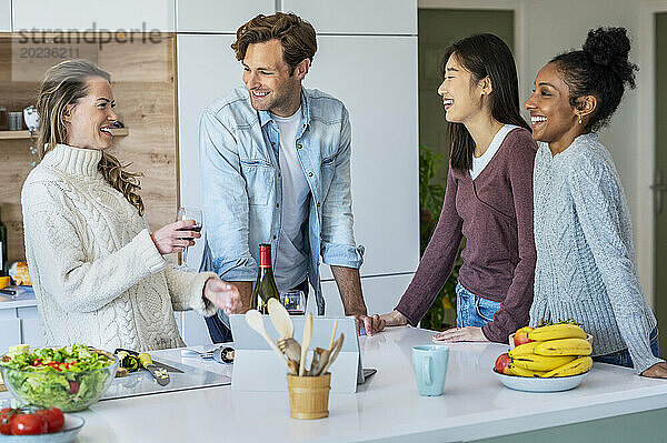 Eine Gruppe von Freunden trinkt Wein  während sie in der Küche hängen