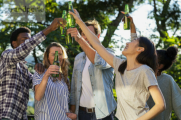 Eine Gruppe von Freunden prostet mit Bierflaschen zu  die draußen stehen