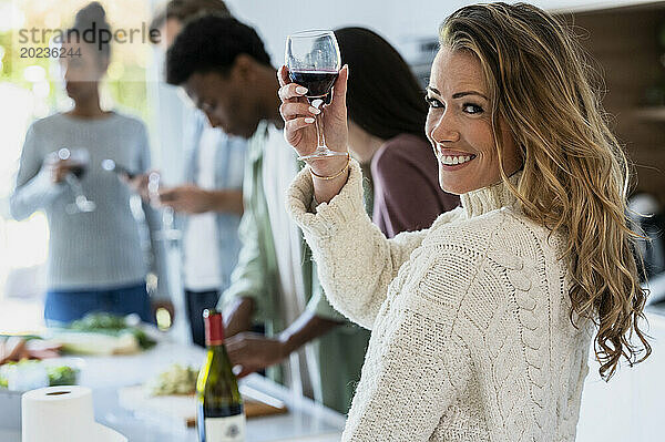 Fröhliche erwachsene Frau blickt zurück in die Kamera  während sie ein Weinglas hebt