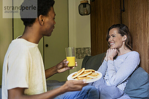Glückliche Frau liegt im Bett  während Freunde sie mit Frühstück überraschen