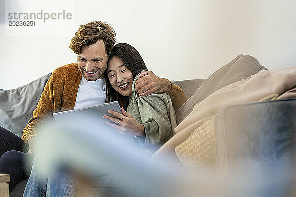 Erwachsenes Paar kuschelte sich  während es im Wohnzimmer ein digitales Tablet nutzte