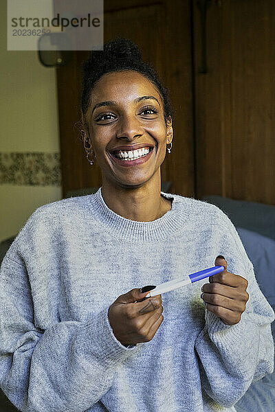 Fröhliche Frau schaut nach oben  während sie einen Schwangerschaftstest hält