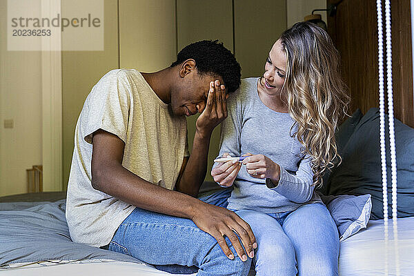 Enttäuschter Mann mit der Hand auf dem Gesicht sitzt neben seiner Freundin und macht einen Schwangerschaftstest
