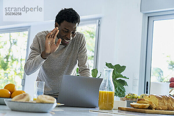 Adult man having a video call on laptop while standing at kitchen counter