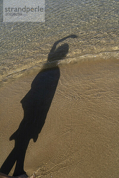 Shadow of unidentified person on sandy beach near water's edge