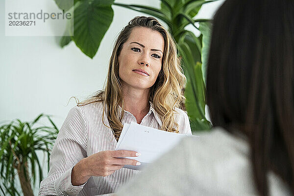 Selbstbewusste Geschäftsfrau hält Papiere in der Hand  während sie mit einem Kollegen spricht