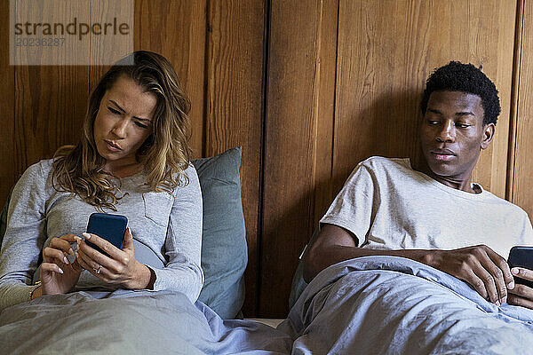 Distrustful boyfriend looking on girlfriend's smart phone while lying on bed