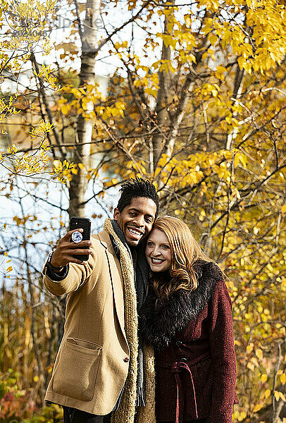Nahaufnahme eines gemischtrassigen Ehepaars  das gemeinsam ein Selfie macht  während es bei einem Familienausflug im Herbst in einem Stadtpark schöne Zeit miteinander verbringt; Edmonton  Alberta  Kanada