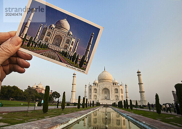 Die Hand eines Mannes hält ein Postkartenfoto des Taj Mahal mit dem echten Taj Mahal dahinter; Agra  Indien